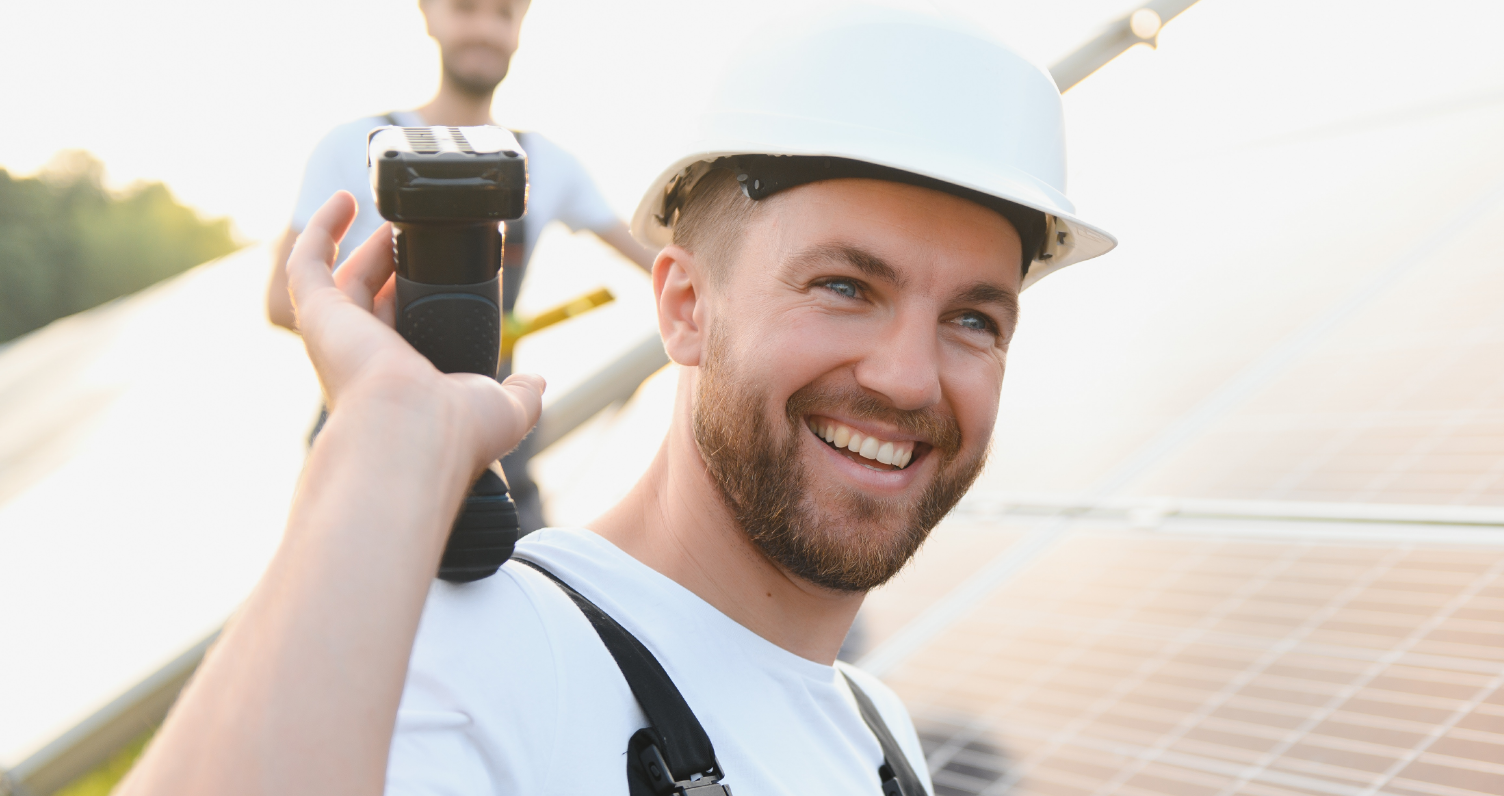 Uśmiechnięty instalator w kasku na tle panel fotowoltaicznych